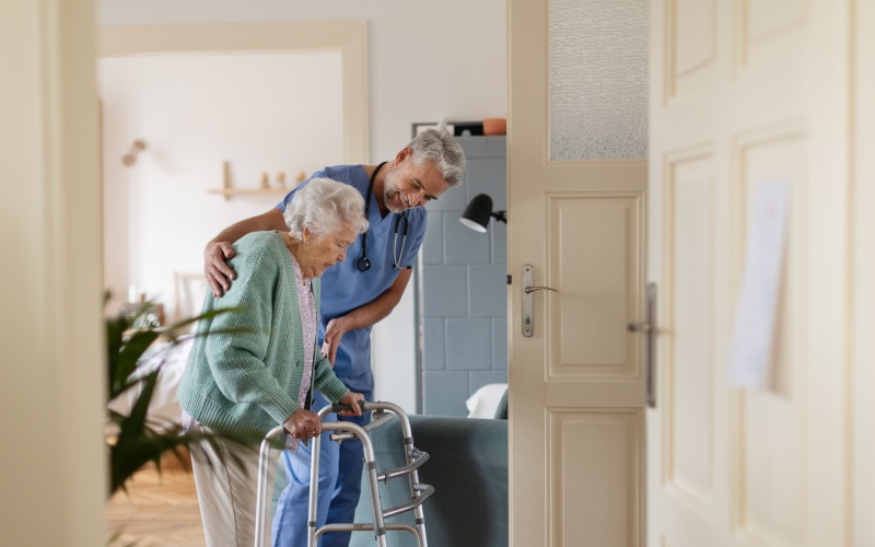 caregiver helping senior woman walk her home thoughful male nurse