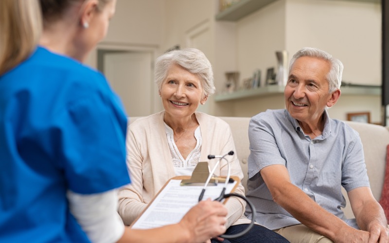 nurse home visit senior couple doctor holding clipboard stethoscope conversation