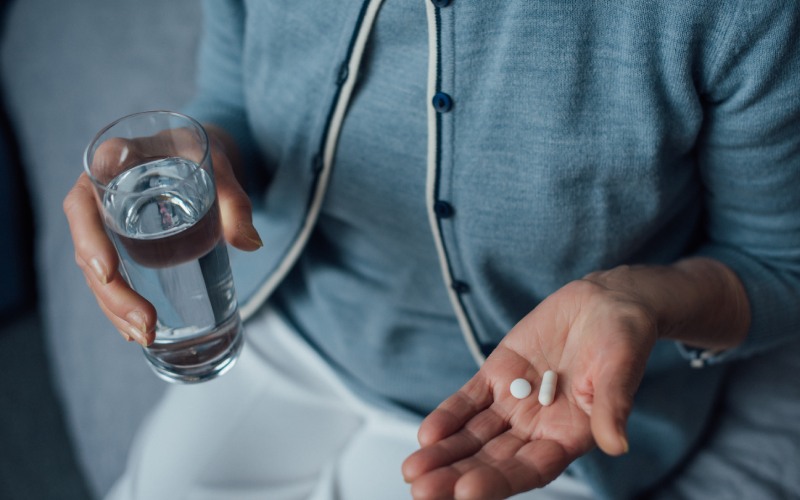 senior woman sitting holding pills glass water home