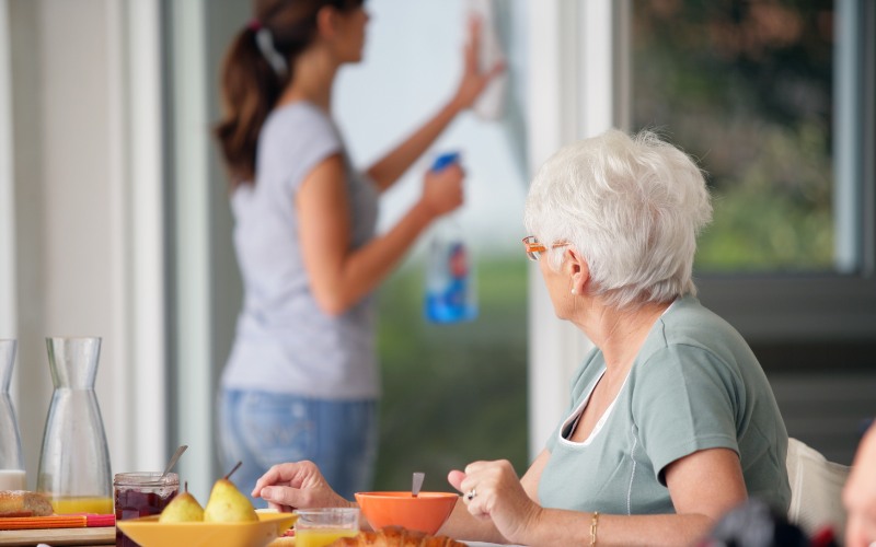senior-woman-having breakfast with home care in the background